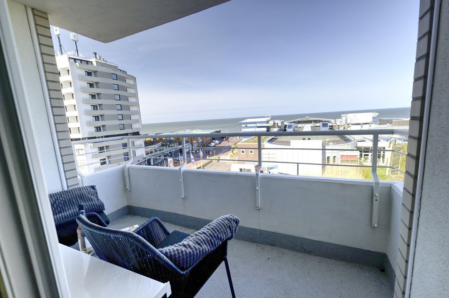 A balcony with a view of the city and the sea, featuring a chair and a table.