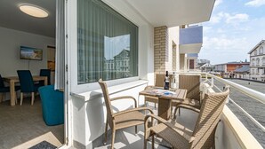 A balcony with wicker furniture, a dining area with a TV, and a view of the cityscape. - Neptun - Wohnen am Meer, in Dieser Zentralen Wohnung (Sylt)