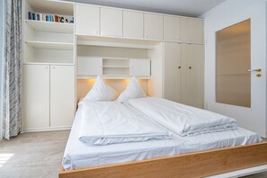 A bedroom with a bed, white bedding, a wooden headboard, a wardrobe with multiple compartments, and a door with a window.