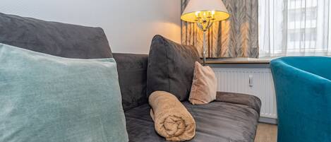 A modern living room with a grey sofa, teal armchair, and a lamp.