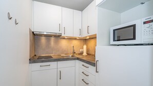 A modern kitchen with white cabinets, a stainless steel range hood, a built-in microwave, and a sink with a faucet. - Neptun - Wohnen am Meer, in Dieser Zentralen Wohnung (Sylt)