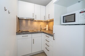 A modern kitchen with white cabinets, a stainless steel range hood, a built-in microwave, and a sink with a faucet.