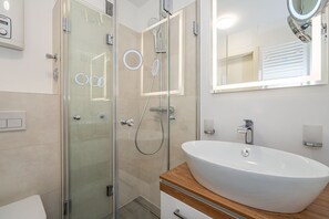 A modern bathroom with a glass shower enclosure, a white sink with a wooden countertop, and a mirror with a round frame. - Neptun - Wohnen am Meer, in Dieser Zentralen Wohnung (Sylt)