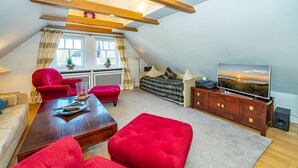 Ein modernes Loft-Apartment mit hohen Decken, freiliegenden Holzbalken, einem gemütlichen roten Sofa, einem Holztisch, einem Fernseher und einem großen Fenster mit Vorhängen.