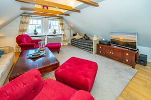 Un loft moderno con techo alto, vigas de madera a la vista, un sofá rojo acogedor, una mesa de centro de madera, un televisor y un ventanal con cortinas.