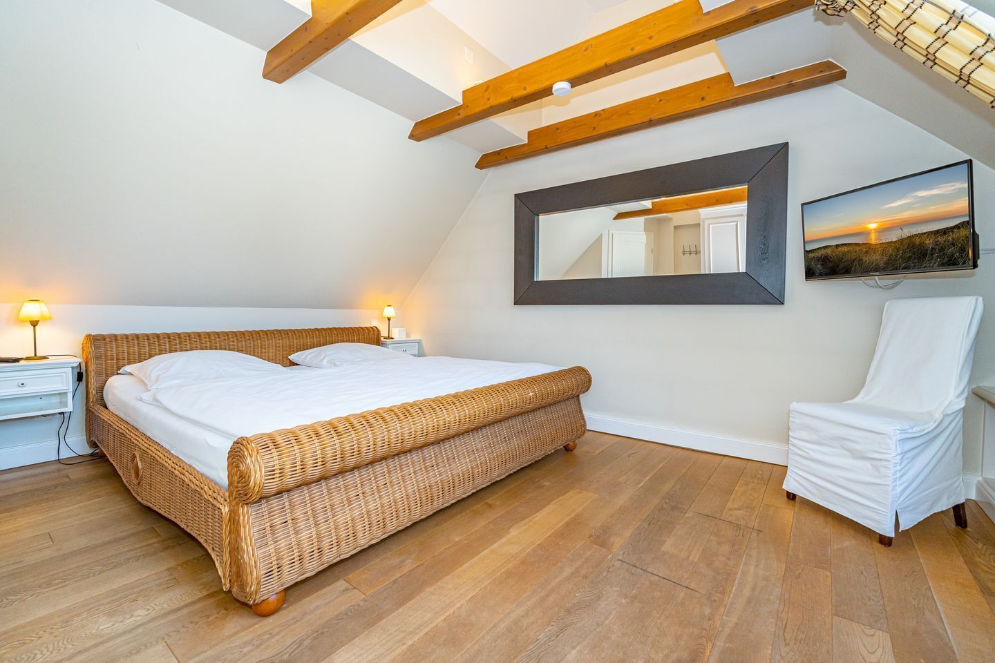 Une chambre à coucher avec un grand lit, une chaise, une table de chevet, un miroir et un tableau accroché au mur.