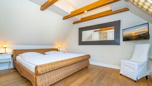 A bedroom with a large bed, a chair, a nightstand, a mirror, and a painting on the wall.