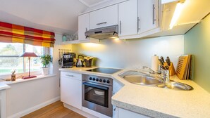 A compact kitchen with white cabinets, a built-in oven, a stovetop, and a sink.