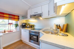 Une cuisine compacte avec des meubles blancs, un four encastré, une plaque de cuisson et un évier.