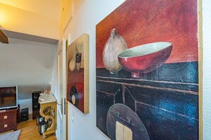 Un pasillo con obras de arte en las paredes, piso de madera y una puerta que da a otra habitación.
