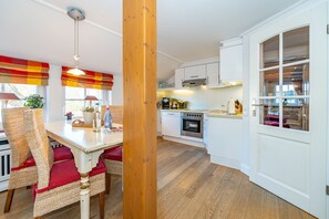 A modern kitchen with white cabinets, a wooden floor, and a dining area with wicker chairs and a red cushion.