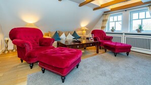 A cozy living room with a high ceiling and exposed beams, featuring a sofa set, a coffee table, and a red ottoman.
