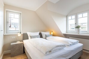A modern bedroom with a large bed, two bedside tables, and a window with a view of buildings.