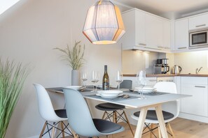 Une cuisine moderne avec des meubles blancs, une table à manger dressée avec des assiettes, des verres et une bouteille, et un luminaire suspendu.