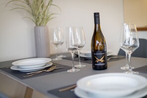 Una mesa de comedor dispuesta con platos, cubiertos y copas de vino, con una botella de vino Schneider Grauburgunder 2020.