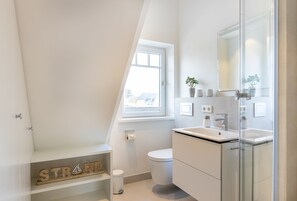 Une salle de bain moderne dotée d’un puits de lumière, de toilettes, d’un lavabo avec un miroir et d’une étagère ornée d’objets décoratifs.
