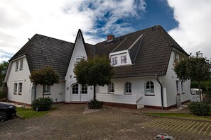 Une maison blanche à deux étages, dotée d’un toit à forte pente, d’un petit porche à l’avant et d’une allée pavée.