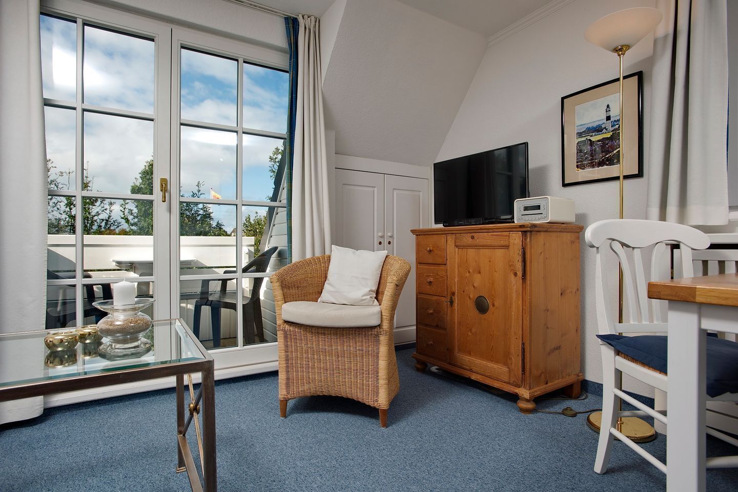 A room with a large window, wicker chair, wooden cabinet, and a television.