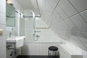 Une salle de bain moderne avec une douche à parois de verre, un lavabo blanc avec une serviette et un tabouret noir.