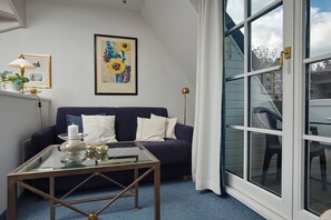 Een moderne woonkamer met een donkerblauwe bank, een glazen salontafel en een groot raam met uitzicht op de omgeving.