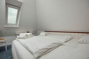 Hotelkamer met een groot bed, een klein nachtkastje met een lamp, en een raam met uitzicht op de lucht.