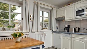 Cozinha com armários brancos, uma mesa de madeira e uma janela com cortinas.