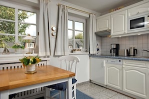 Een keuken met witte kastjes, een houten tafel en een raam met gordijnen.