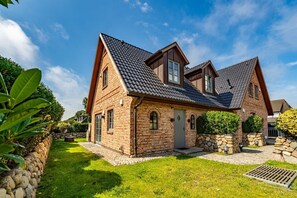 Une maison à deux étages, construite en briques, avec un toit en pente, des fondations en pierre et une pelouse bien entretenue.