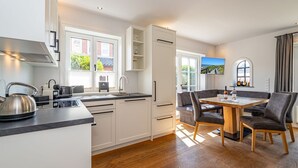 Una cocina moderna con estufa integrada, una zona de comedor con mesa y sillas de madera, y vistas a zonas verdes a través de las ventanas.