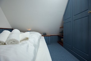A bedroom with a bed, rolled white towels, a nightstand, a lamp, and a blue wardrobe.