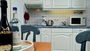 Une cuisine avec des meubles blancs, un four à micro-ondes, une bouilloire et une bouteille d’eau posée sur un plateau.