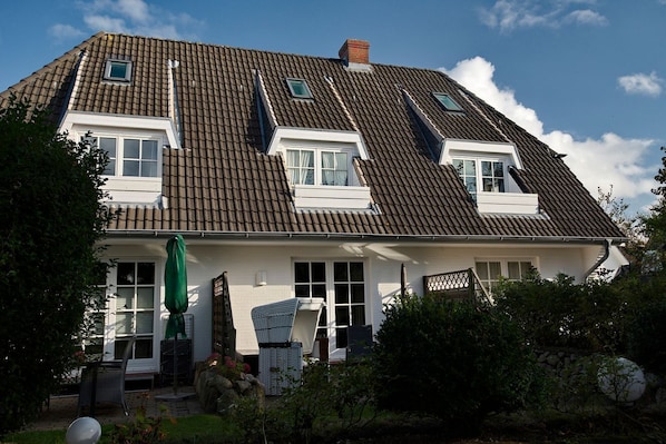 A two-story house with a sloped roof, dormer windows, and a front porch with outdoor seating.