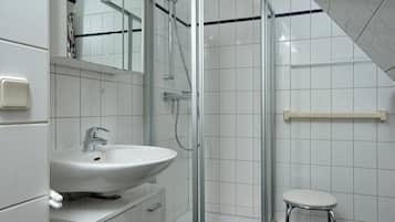 Ein modernes Badezimmer mit einer Duschkabine aus Glas, einem weißen Waschbecken und einem kleinen Hocker.