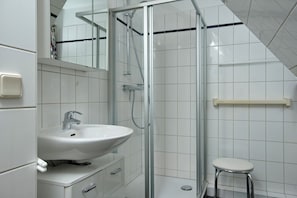 A modern bathroom with a glass-enclosed shower, a white sink, and a small stool.