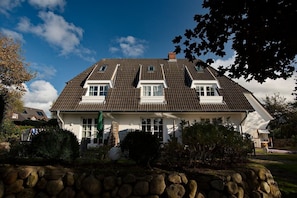 A two-story house with a sloped roof, dormer windows, and a stone wall in the foreground.