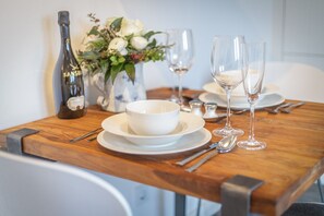 A dining table set with white plates, bowls, wine glasses, and cutlery. A bottle of wine and a vase with flowers are also visible.