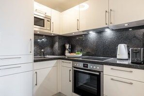 Een moderne keuken met witte kasten, een zwart granieten aanrecht, een magnetron, een koffiezetapparaat, een broodrooster en een oven.
