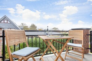 Un balcon avec deux chaises en bois et une table, une bouteille et un carnet.
