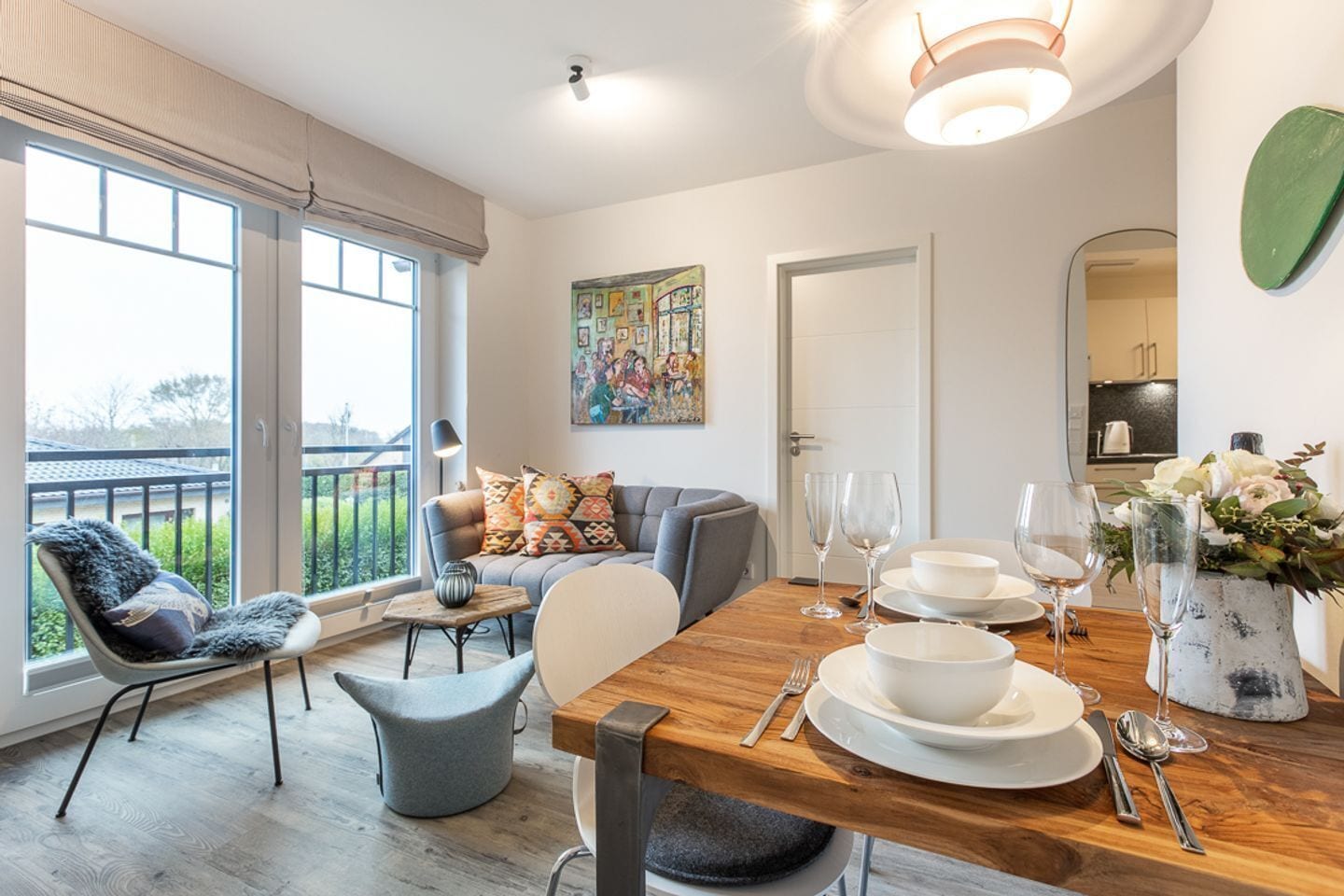 A modern dining area with a wooden table set for four, a grey sofa, and a balcony with a view.