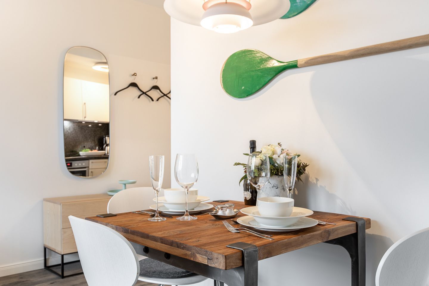A dining area with a wooden table set for two, a mirror, and a green paddle on the wall.