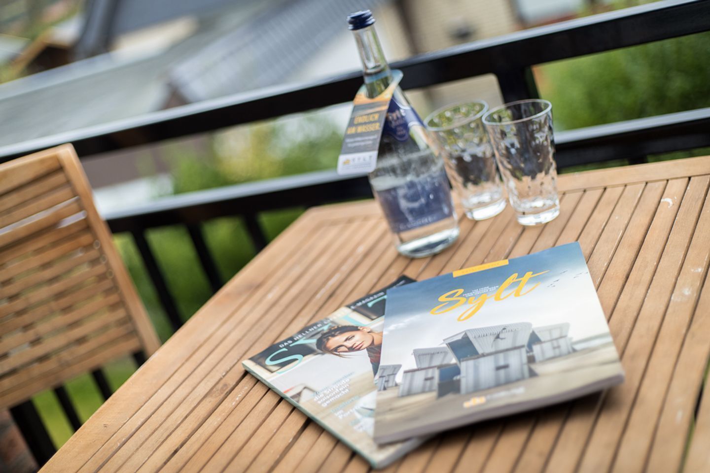 A wooden table with a bottle of whiskey, three glasses, and a magazine on it.