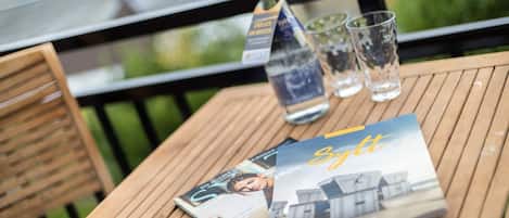 A wooden table with a bottle of whiskey, three glasses, and a magazine on it.