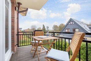 Un balcon avec une table et des chaises en bois, une bouteille et un verre.