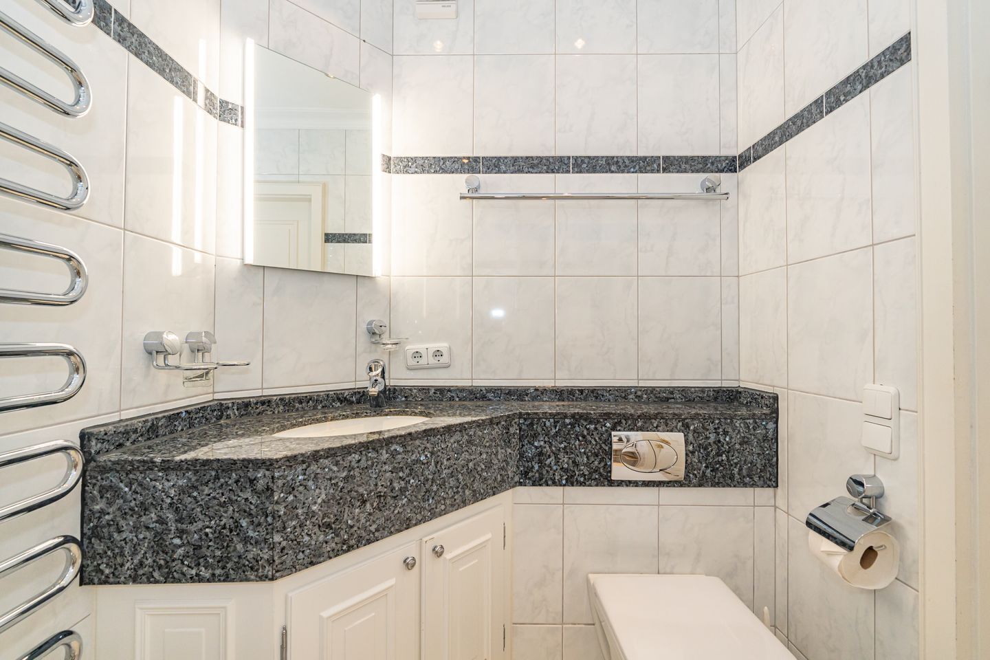 A modern bathroom with a granite countertop, a sink, a toilet, and a mirror.