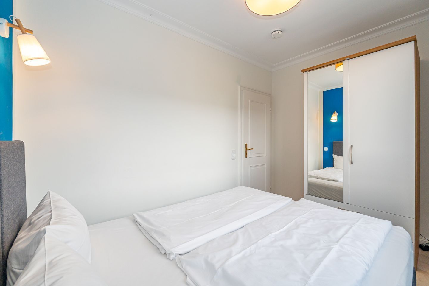 Une chambre d’hôtel avec un lit, une armoire, une porte et un luminaire fixé au mur.