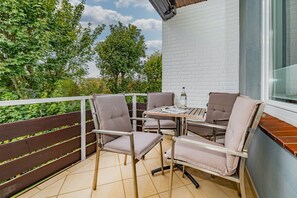 Een balkon met een tafel, stoelen, een fles en een tijdschrift.