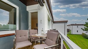 Ein Balkon mit Tisch und Stühlen, Blick auf eine grüne Rasenfläche, und ein weißes Gebäude im Hintergrund.