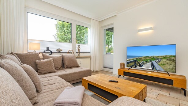 Ein modernes Wohnzimmer mit einer großen Eckcouch, einem Holztisch und einem Flachbildfernseher auf einem Holzboden.