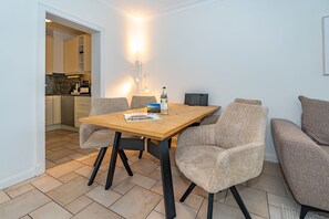A dining area with a wooden table, four upholstered chairs, a bottle of wine, and a magazine.