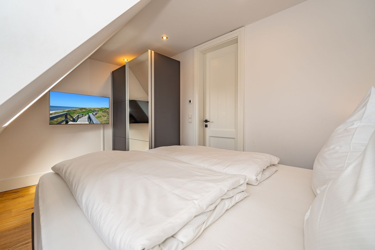 Une chambre à coucher avec un lit, une porte blanche et un téléviseur fixé au mur qui diffuse une vue panoramique.